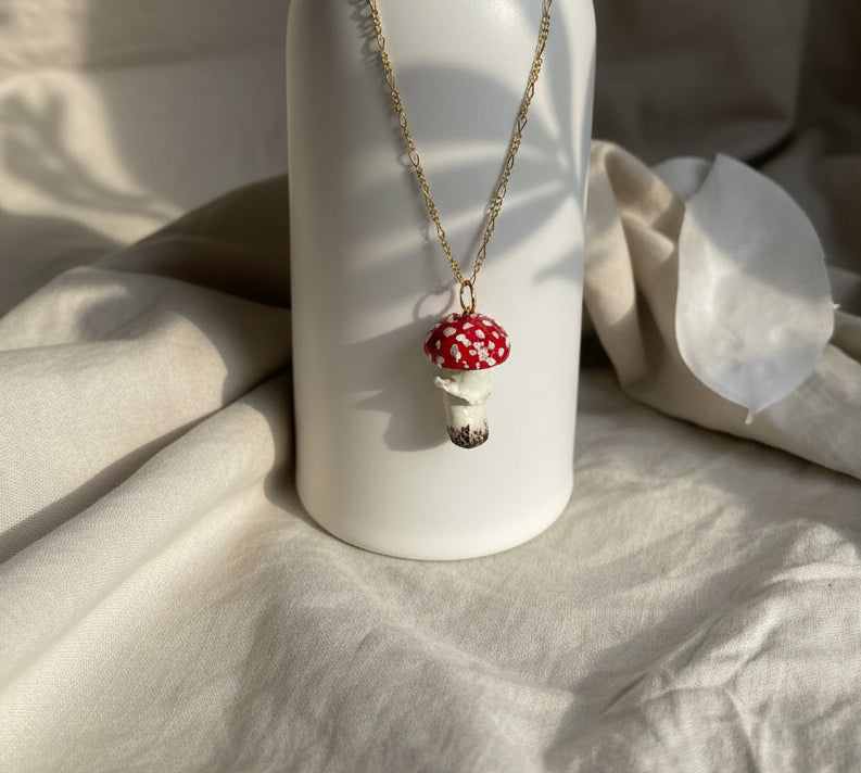 Mushroom-shaped pendant necklace on a white cylindrical object with a beige fabric background