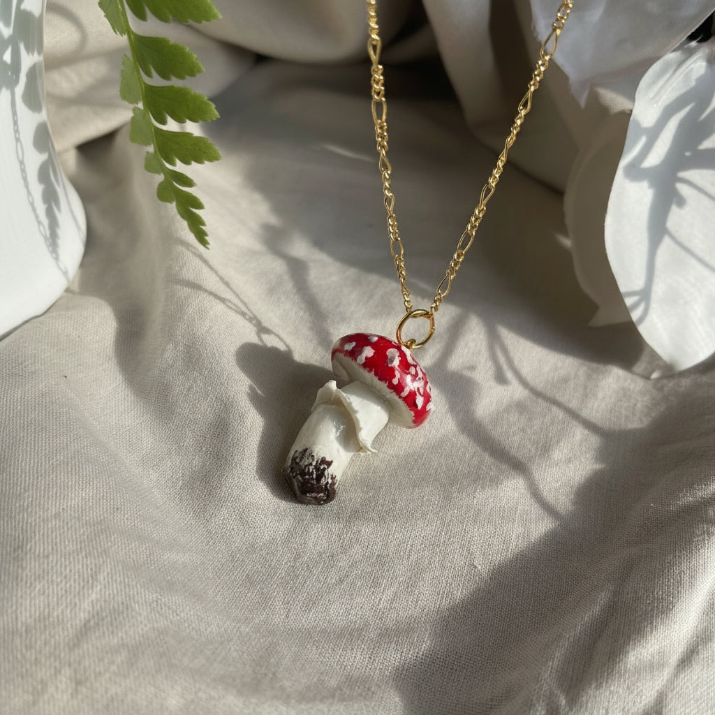 Mushroom-shaped pendant on a gold chain against a light fabric background