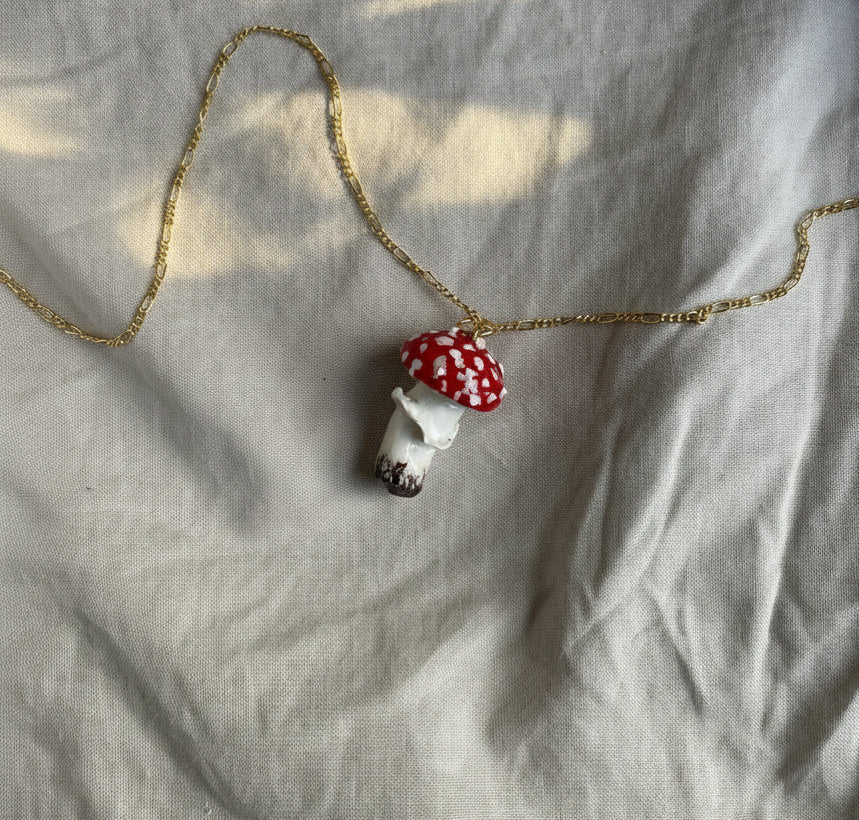 Mushroom-shaped pendant on a gold chain against a textured fabric background